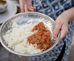 Hands holding a tin plate filled with rice and curry